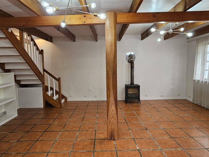 Spacious living area featuring exposed timber beams, terracotta floor tiles, a central timber support column, and a cast iron fireplace.