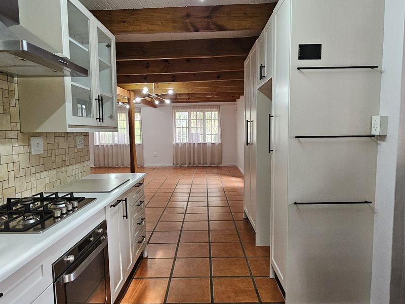 Spacious open-plan kitchen and living area featuring tiled floors, exposed timber ceiling beams, and modern white cabinetry with integrated appliances.