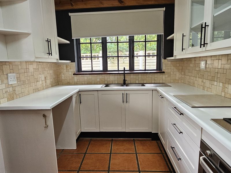 A well-maintained kitchen featuring white cabinetry, stone tile backsplash, gas hob, built-in oven, and terracotta floor tiles.