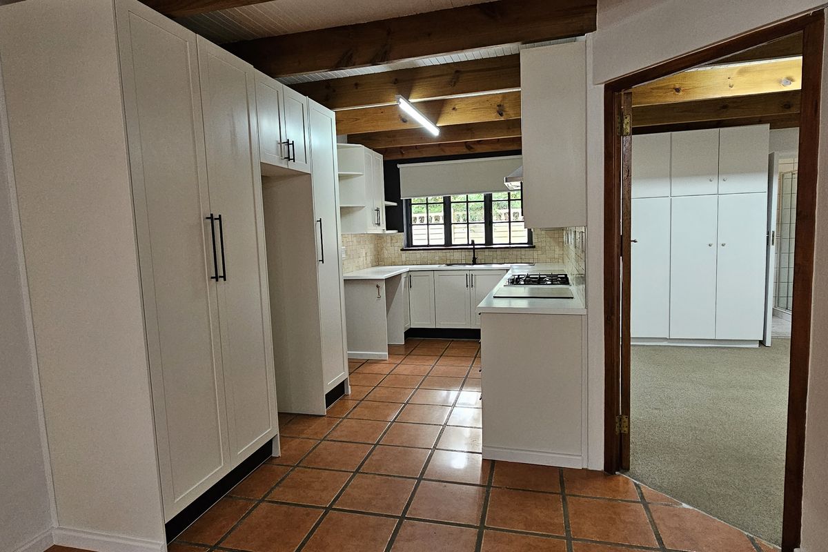 A clean, functional kitchen featuring white cabinetry, gas hob, tiled flooring, and exposed timber ceiling beams, offering a bright and practical workspace.