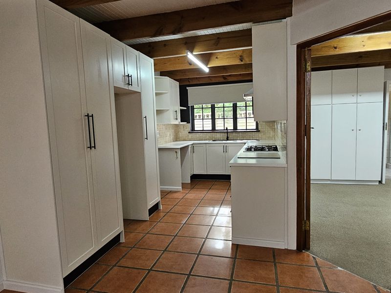 A clean, functional kitchen featuring white cabinetry, gas hob, tiled flooring, and exposed timber ceiling beams, offering a bright and practical workspace.