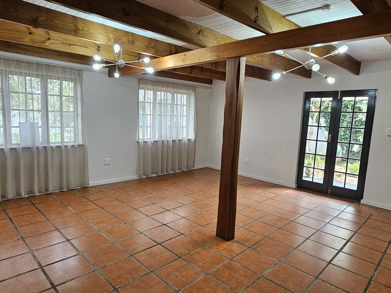 Spacious living area featuring exposed timber ceiling beams, terracotta floor tiles, a wood-burning fireplace, and direct access to the garden through french doors.