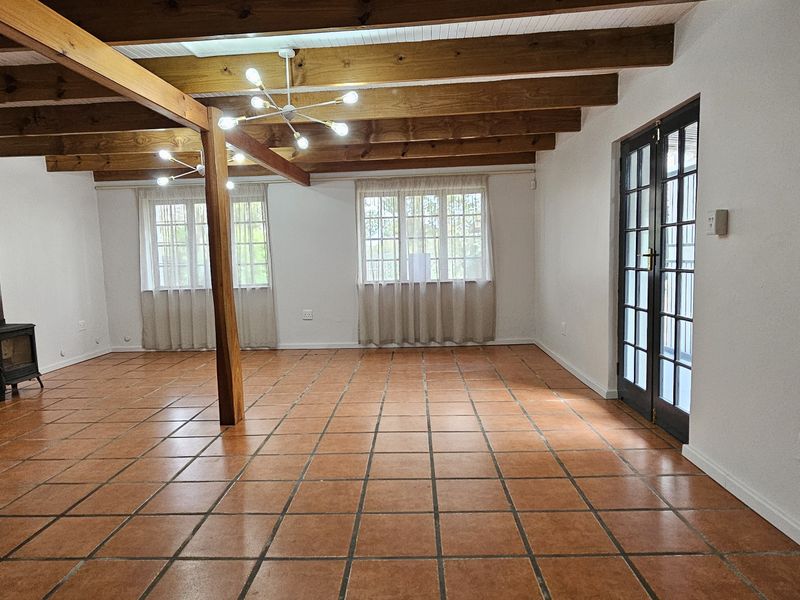 Spacious living area featuring exposed timber ceiling beams, terracotta floor tiles, and a cozy wood-burning fireplace, with direct access to the outdoors via french doors.