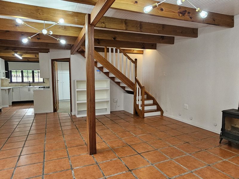 Spacious open-plan living area featuring exposed timber beams, terracotta flooring, a wood-burning fireplace, and an adjoining kitchen with built-in cabinetry.