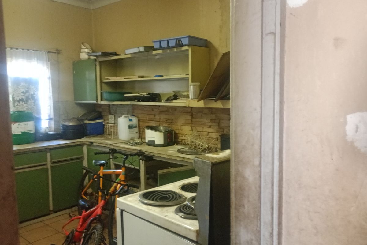 A dated kitchen area featuring built-in cabinetry, a freestanding stove, and tiled splashbacks, requiring significant renovation and modernization.