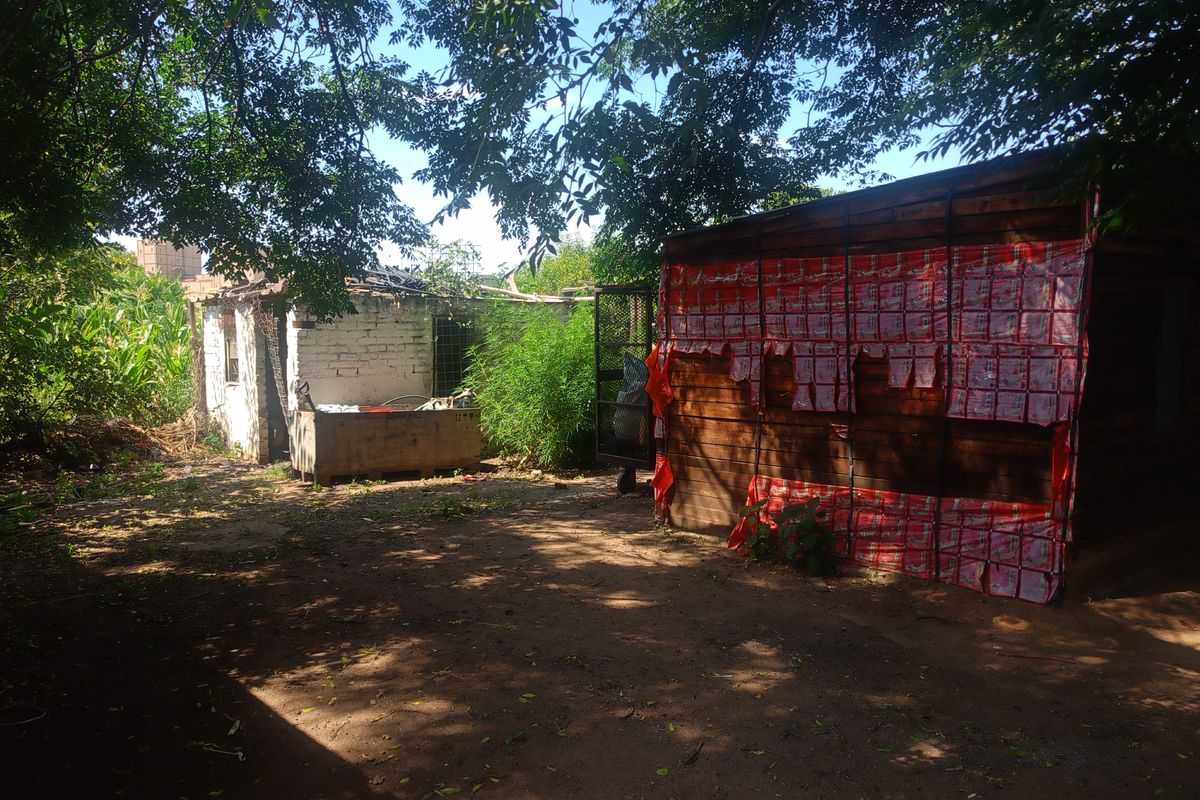 Exterior view of a small holding featuring a dilapidated outbuilding with significant structural damage and a secondary wooden structure with temporary coverings.