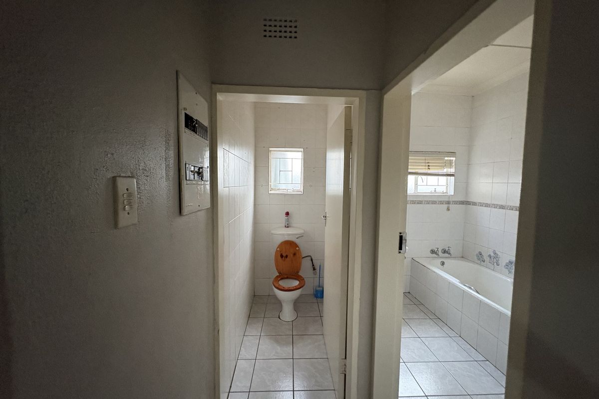 A view from the hallway into a separate toilet and a tiled bathroom featuring a built-in bathtub and ceramic wall tiling.