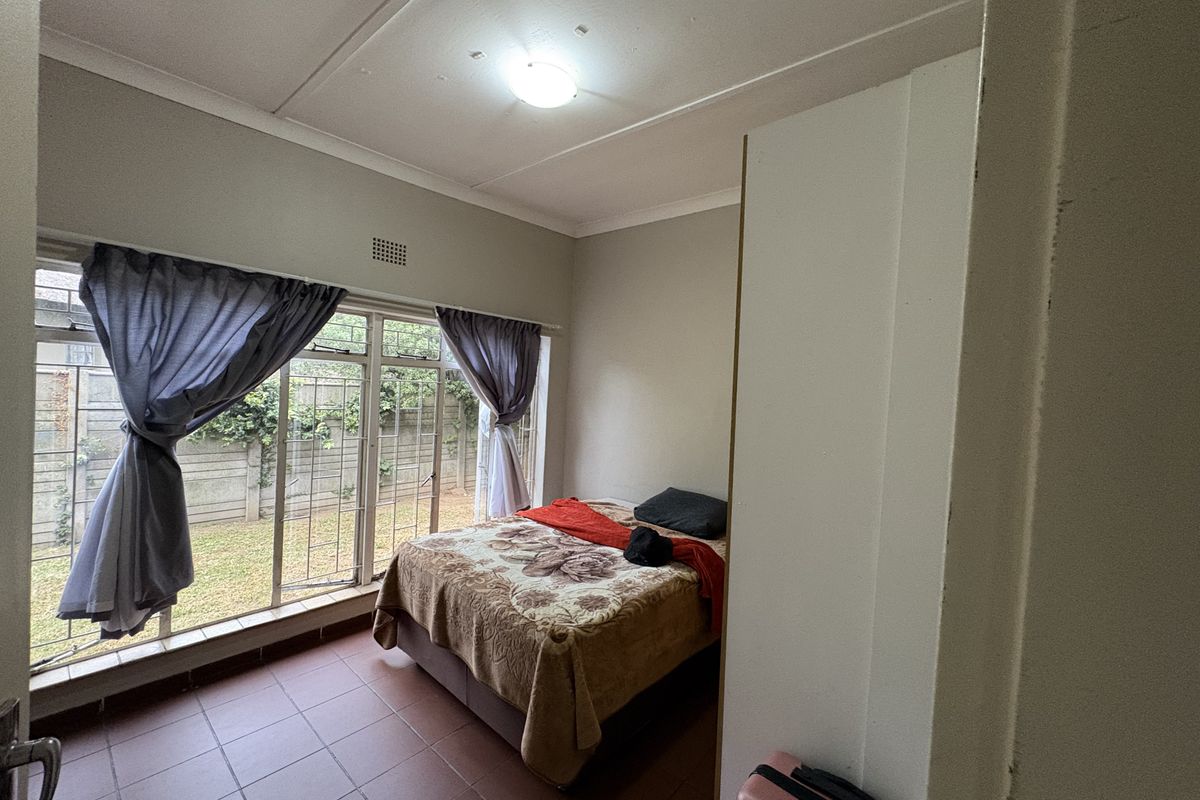 A bedroom featuring tiled flooring, large windows with security bars, and built-in cupboard space, offering direct access to the rear garden area.
