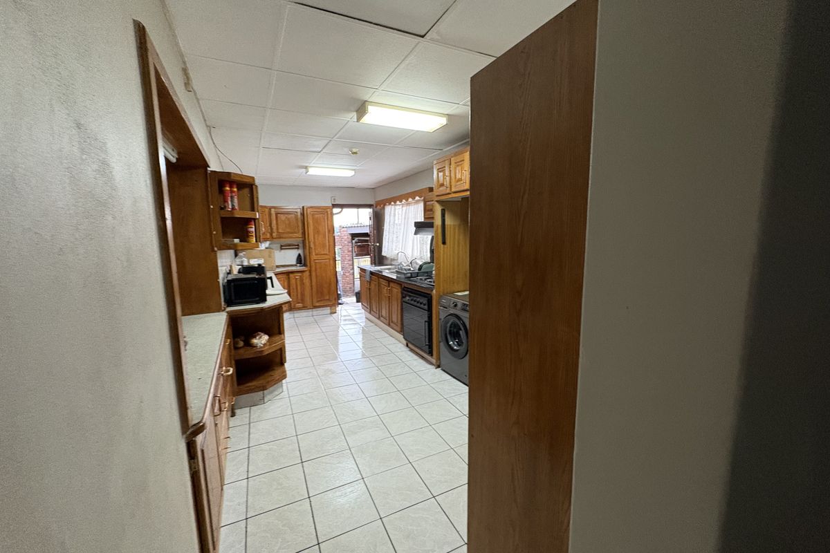 A functional kitchen featuring wooden cabinetry, tiled flooring, and integrated appliances, providing a practical workspace with direct access to the rear exterior.