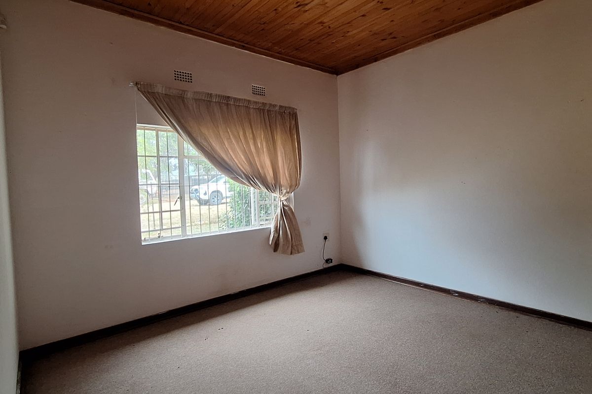 An empty bedroom featuring a timber-clad ceiling, carpeted flooring, and a window with security bars.
