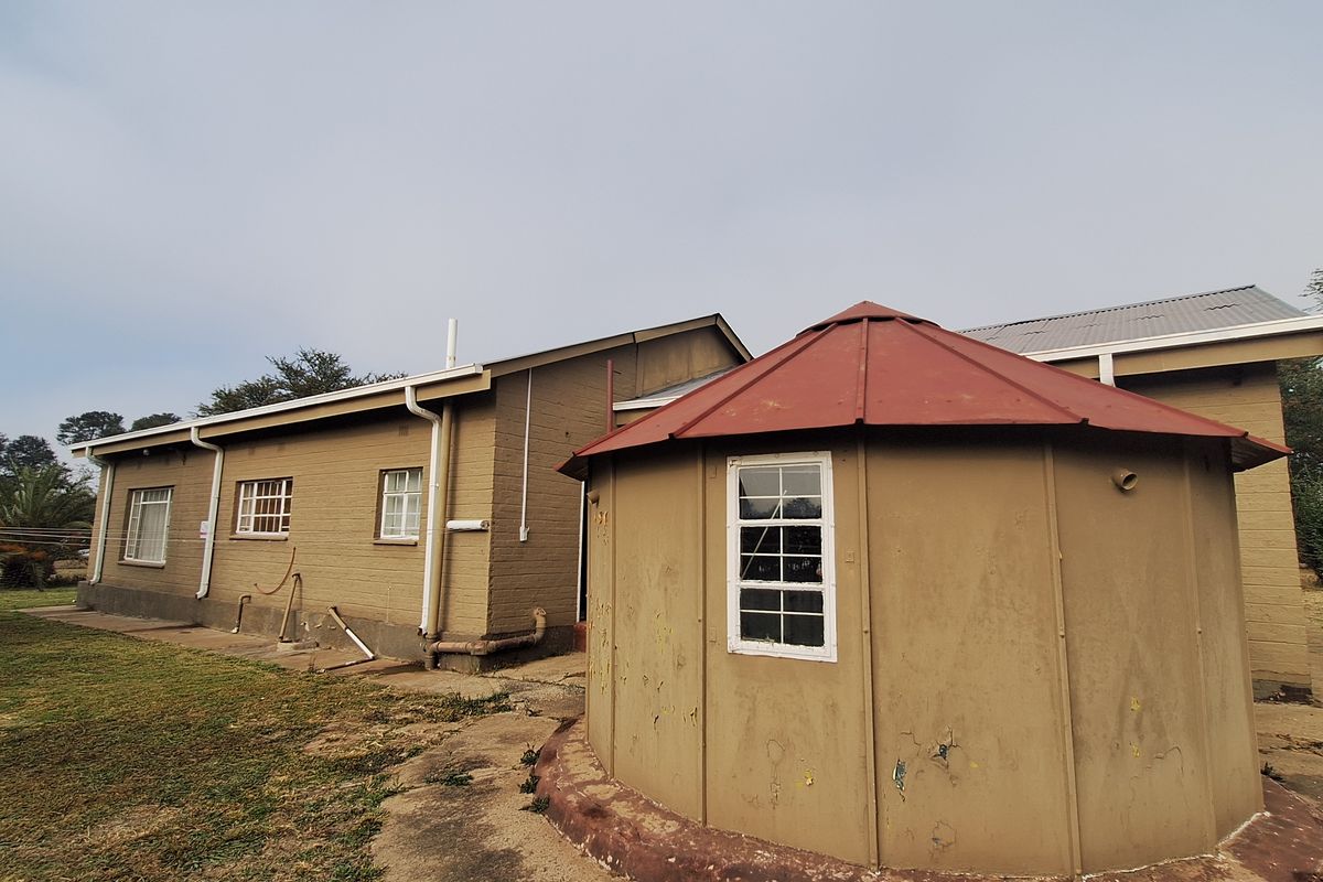 Rear view of the property featuring a unique circular structure with a red metal roof and adjacent main building with brick exterior.