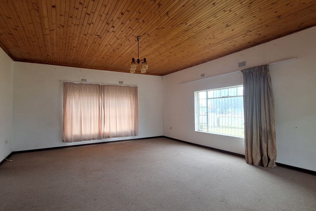 Spacious living room featuring a traditional timber-clad ceiling, large windows with security bars, and neutral carpeting throughout.