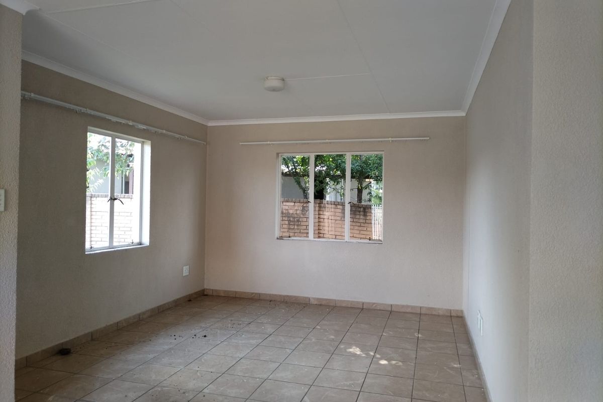 A vacant living room featuring neutral wall tones, tiled flooring, and large windows providing natural light.