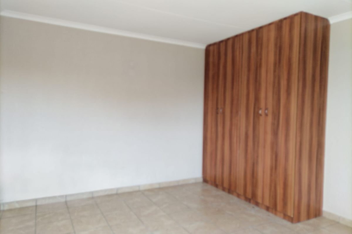 A vacant bedroom featuring neutral walls, tiled flooring, and floor-to-ceiling built-in wooden cupboards.