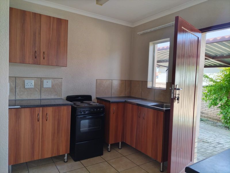 A functional kitchen featuring wood-look cabinetry, tiled splashbacks, a freestanding stove, and direct access to the outdoor area.