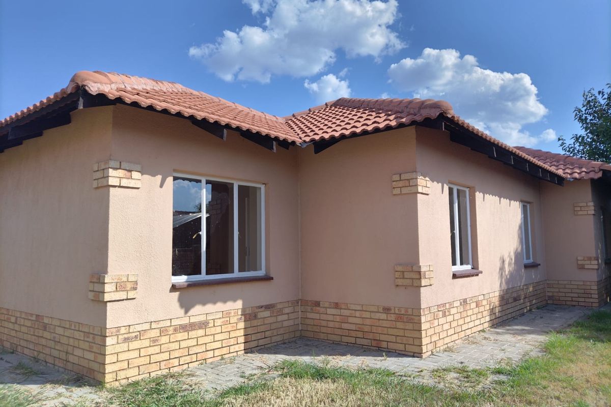 A well-maintained exterior rear view of the house featuring terracotta roof tiles, brick accents, and plastered walls with paved surrounding pathways.