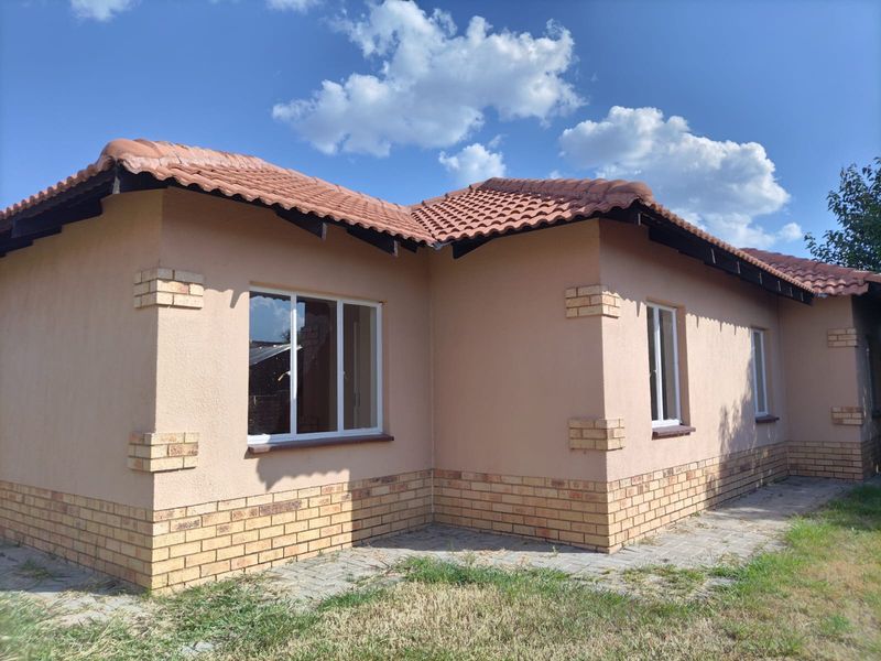 A well-maintained exterior rear view of the house featuring terracotta roof tiles, brick accents, and plastered walls with paved surrounding pathways.