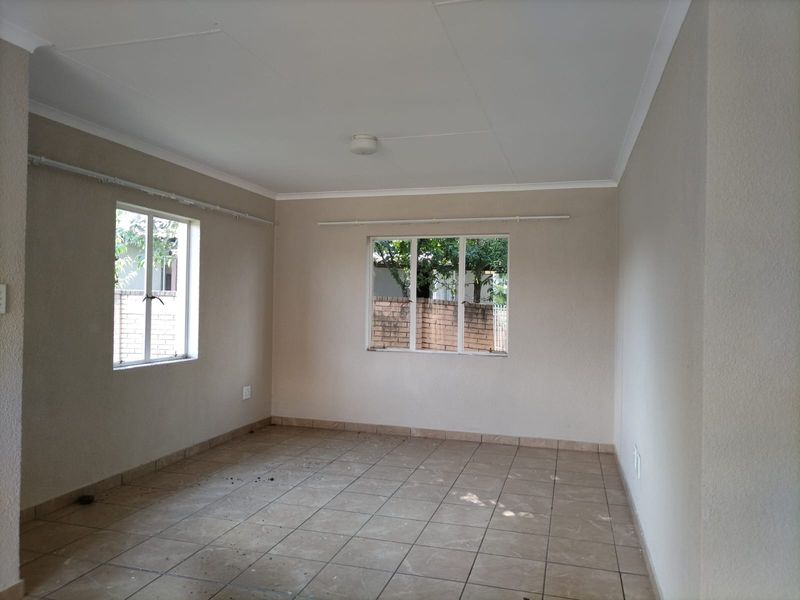 A vacant living room featuring neutral wall tones, tiled flooring, and large windows providing natural light.