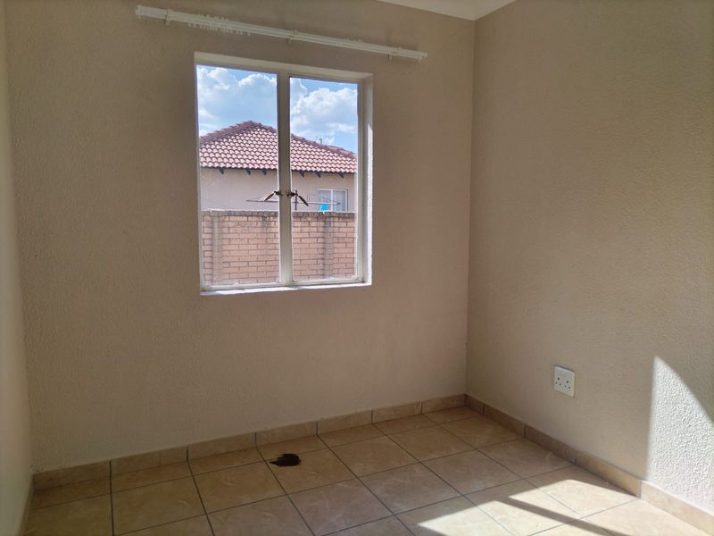 An empty bedroom featuring neutral wall paint, tiled flooring, and a window with a curtain rail.