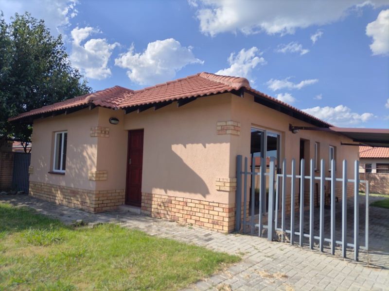 A well-maintained single-story house featuring a tiled roof, brick accents, paved driveway, and secure steel fencing.