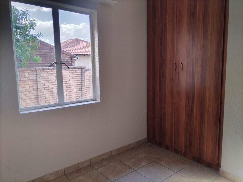 A clean, empty bedroom featuring tiled flooring and a built-in wooden wardrobe, offering a neutral space ready for personalization.