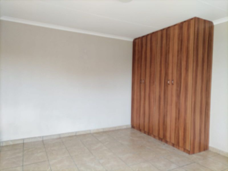 A vacant bedroom featuring neutral walls, tiled flooring, and floor-to-ceiling built-in wooden cupboards.