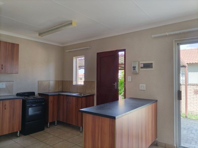 A functional kitchen featuring laminate cabinetry, dark countertops, a freestanding stove, and tiled flooring with direct access to the exterior.