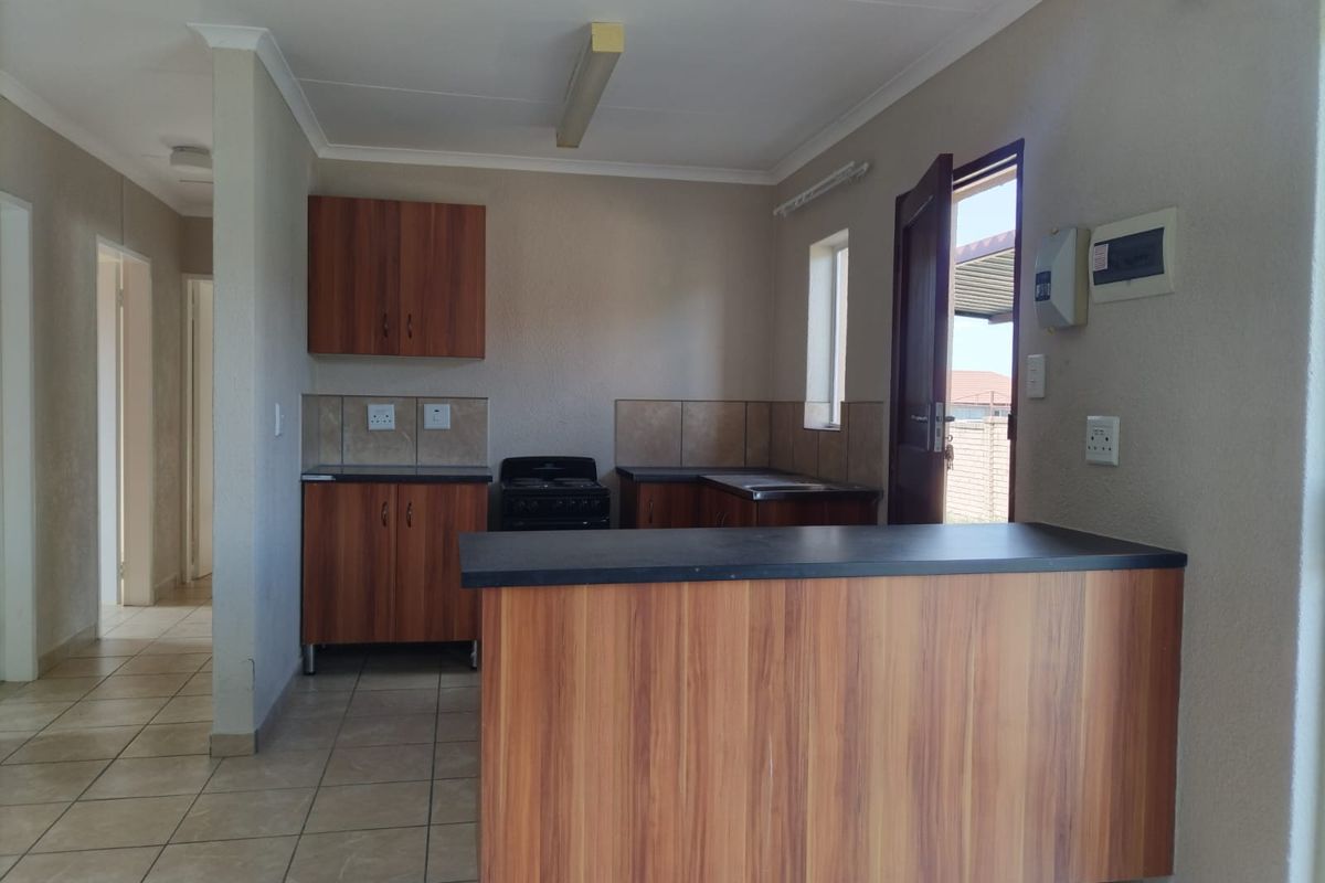 A functional kitchen featuring wood-look cabinetry, laminate countertops, a freestanding stove, and tiled flooring, with direct access to the exterior.