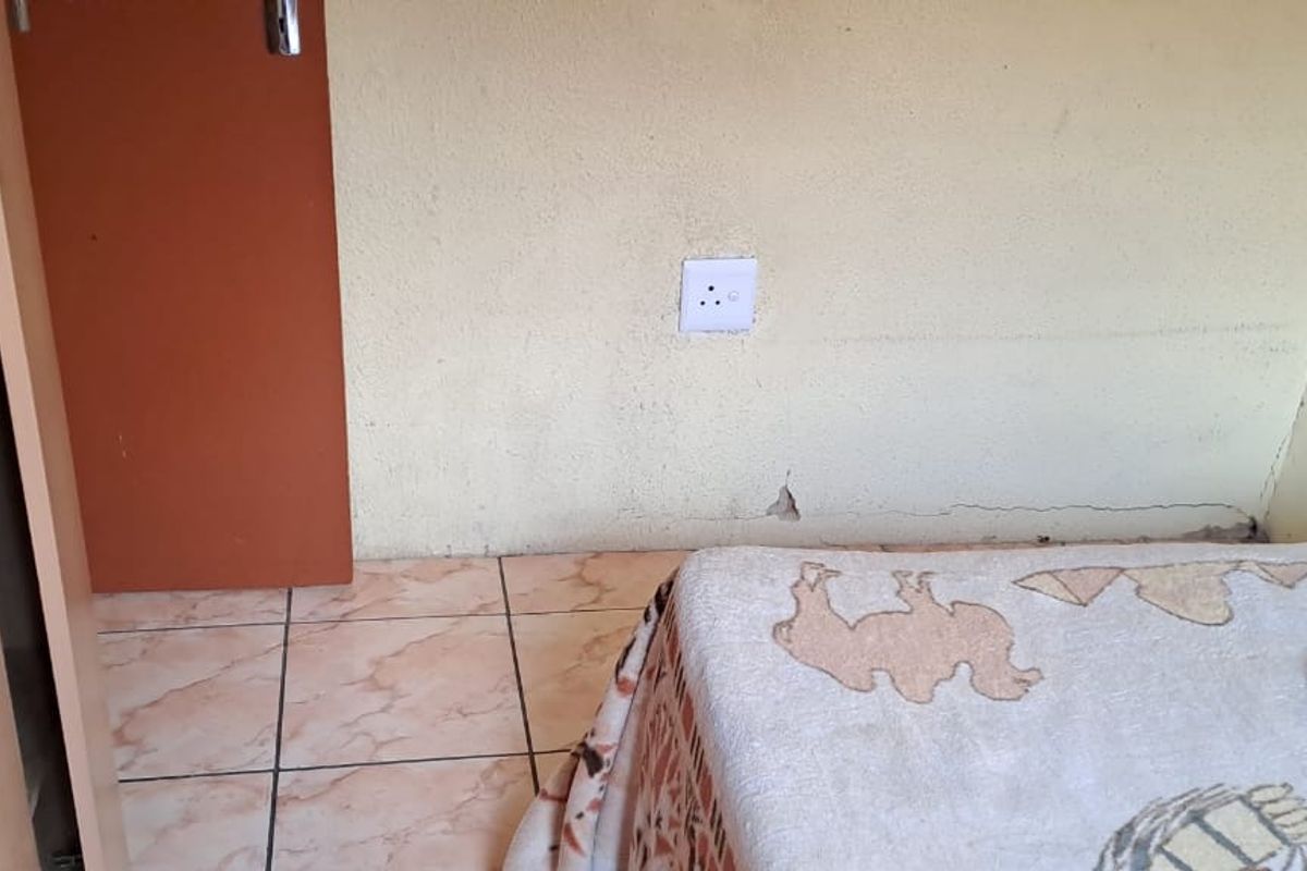 A bedroom interior featuring tiled flooring and a built-in cupboard, showing visible signs of wall damage and plaster cracking.
