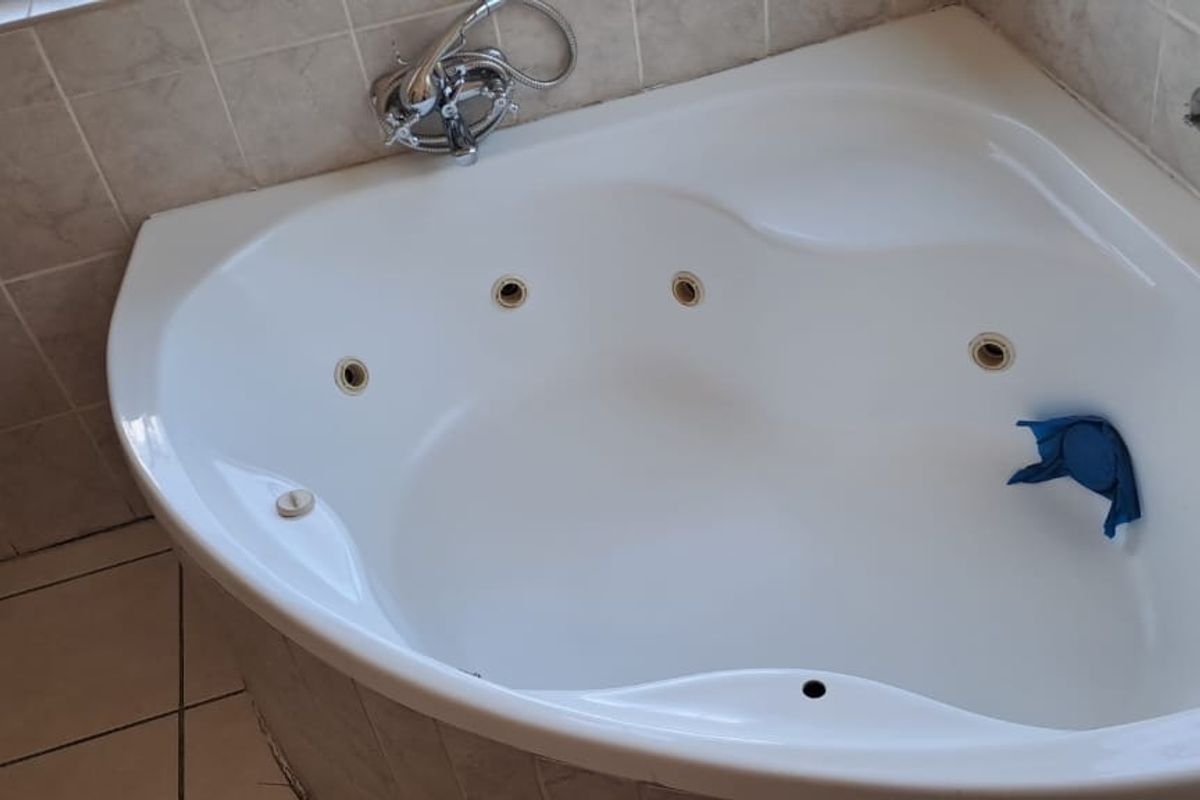 A corner spa bath featuring ceramic tiling and chrome fixtures, currently showing signs of wear with missing jet components.