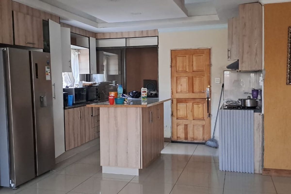 A functional kitchen featuring wood-look cabinetry, a central island, tiled flooring, and a built-in hob with an extractor fan.