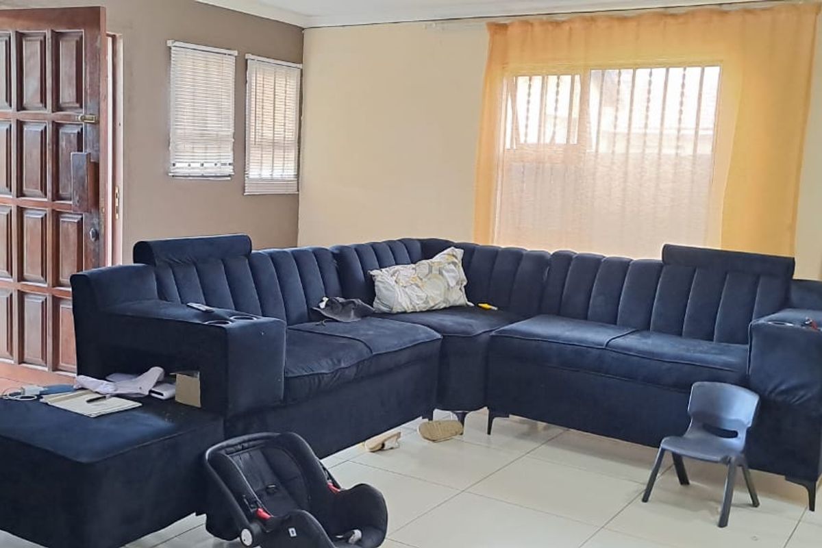 A living room featuring tiled flooring, a timber panelled entrance door, and windows fitted with security bars.