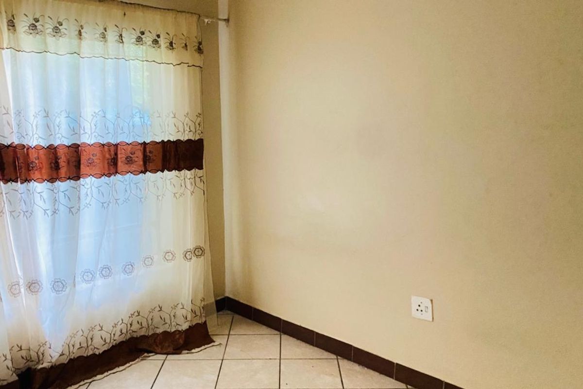 A simple, empty bedroom featuring tiled flooring, neutral walls, and a window with curtains.