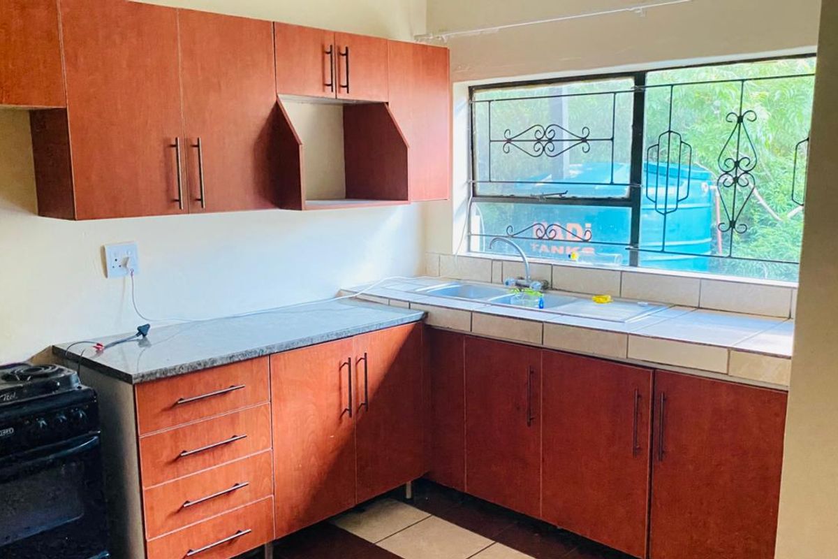A functional kitchen featuring wood-look cabinetry, tiled countertops, a double bowl sink, and security bars on the window.