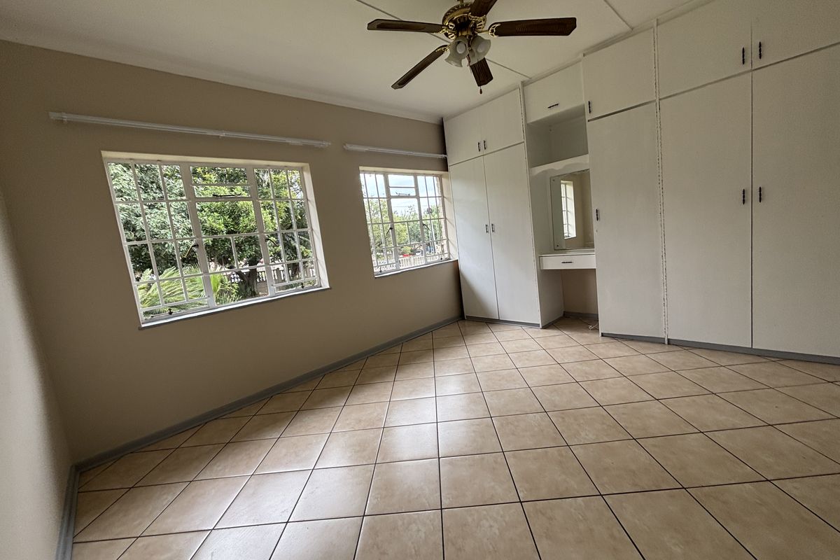 A spacious bedroom featuring built-in wardrobes with a vanity area, tiled flooring, and a ceiling fan, offering a bright and functional living space.
