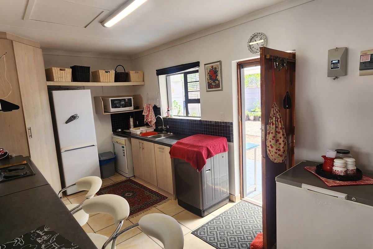 A functional kitchen featuring light wood-finish cabinetry, dark countertops, a tiled splashback, and direct access to the rear exterior.