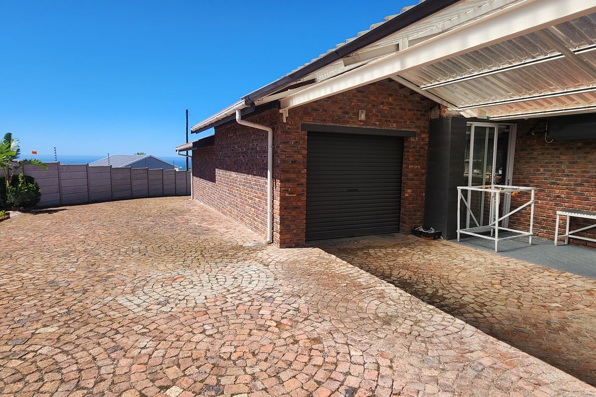Exterior view of a brick-faced garage with a covered patio area and paved driveway, featuring a perimeter wall and partial sea view.