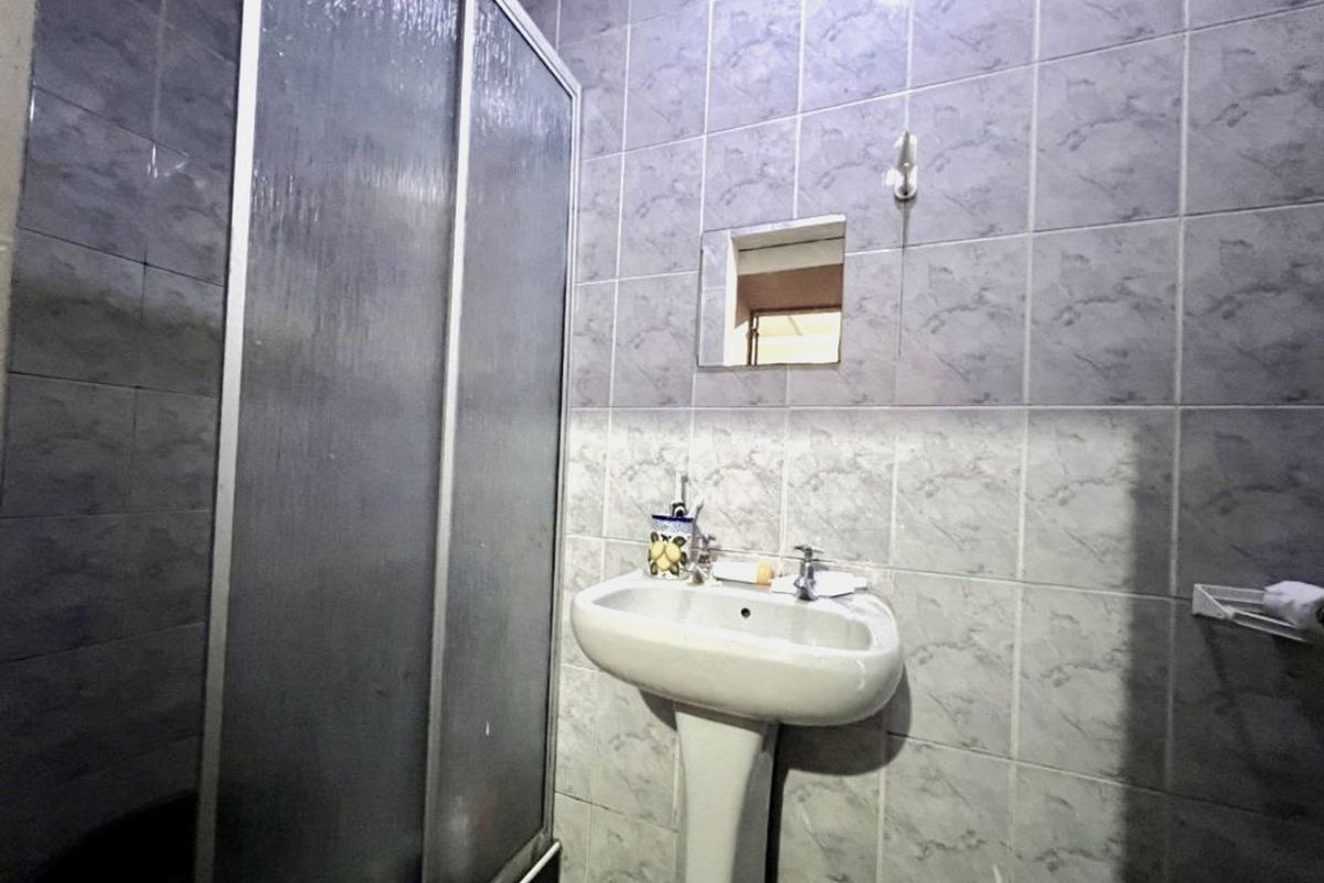 A compact bathroom featuring a pedestal basin, a shower enclosure with sliding doors, and full-height wall tiling.
