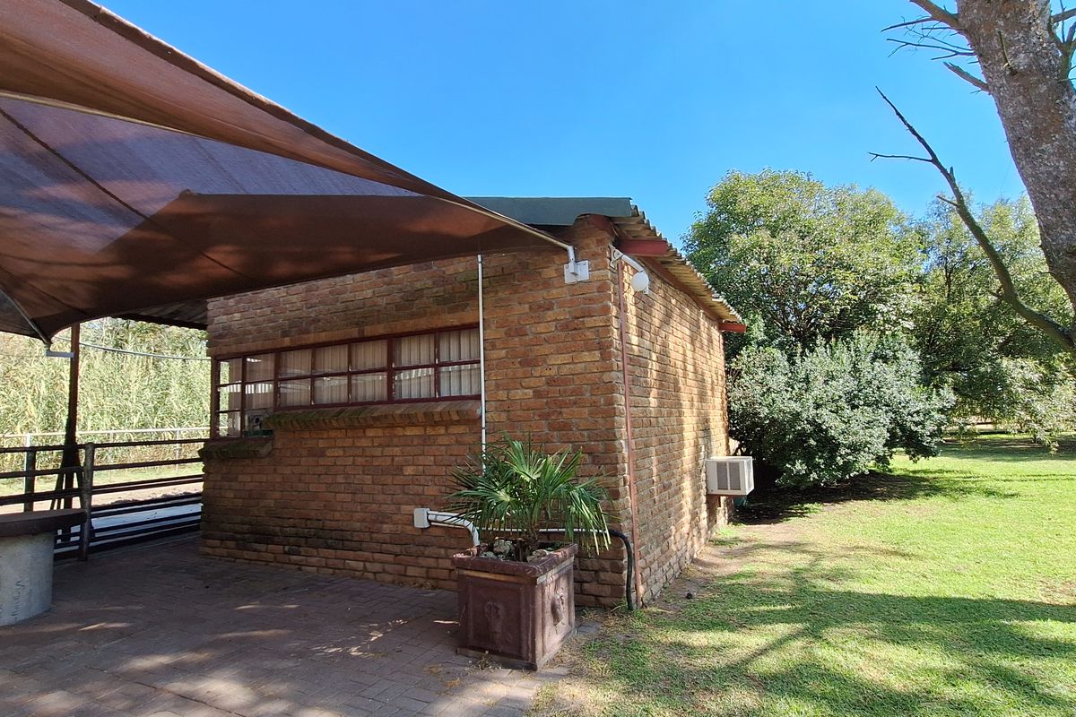 A rustic brick outbuilding featuring a covered patio area with a shade sail, set within a spacious garden on the farm property.