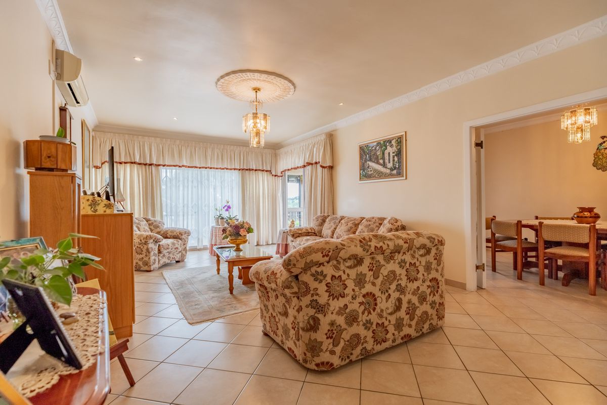 Spacious living room featuring ceramic floor tiles, decorative ceiling rose with chandelier, and a wall-mounted split system air conditioner.
