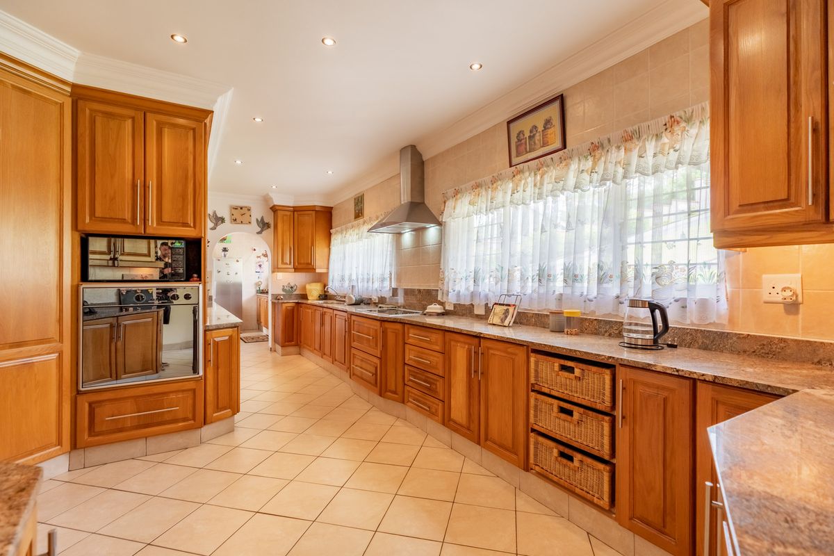 Spacious kitchen featuring extensive wooden cabinetry, granite countertops, built-in oven, stainless steel extractor fan, and ceramic tile flooring.