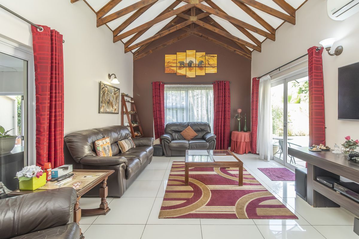 Spacious living room featuring a high vaulted ceiling with exposed timber trusses, large sliding glass doors, and polished tiled flooring.