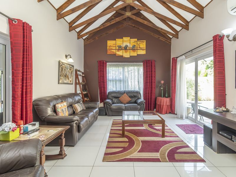 Spacious living room featuring a high vaulted ceiling with exposed timber trusses, large sliding glass doors, and polished tiled flooring.