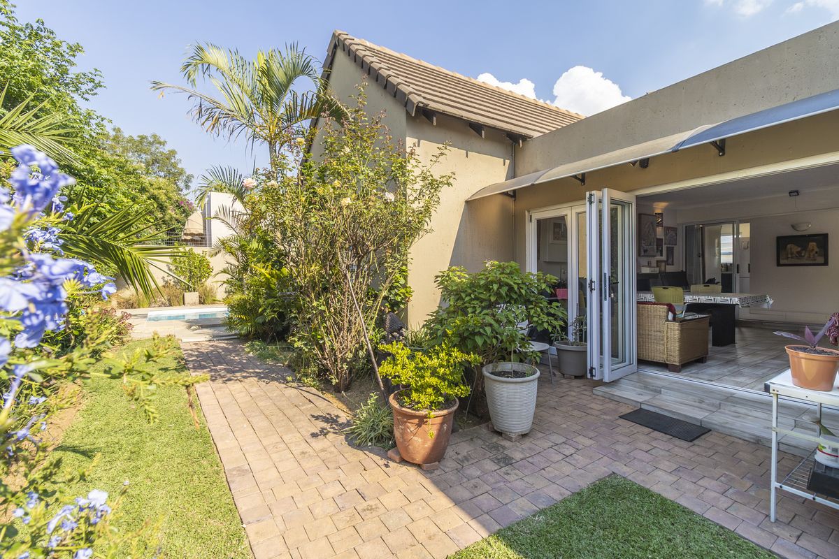 Rear view of the property featuring a paved patio area, bi-fold doors leading to the interior, and a landscaped garden with a swimming pool.