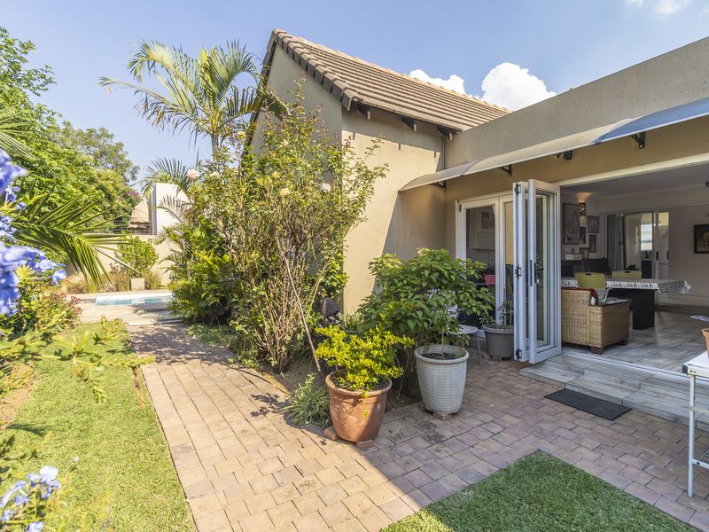 Rear view of the property featuring a paved patio area, bi-fold doors leading to the interior, and a landscaped garden with a swimming pool.