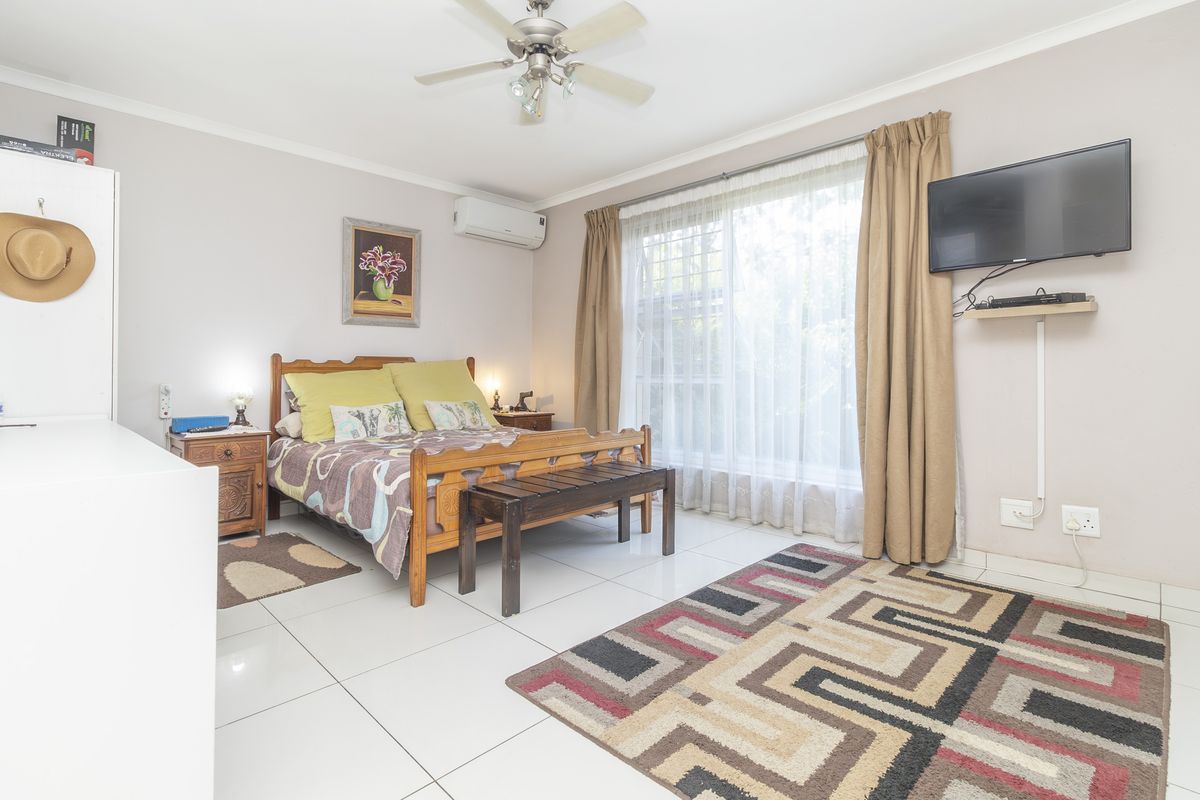 A well-lit bedroom featuring tiled flooring, a ceiling fan, and a wall-mounted air conditioning unit.
