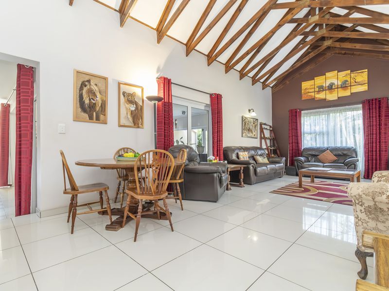 Spacious open-plan living and dining area featuring high vaulted ceilings with exposed timber rafters and polished white floor tiles.