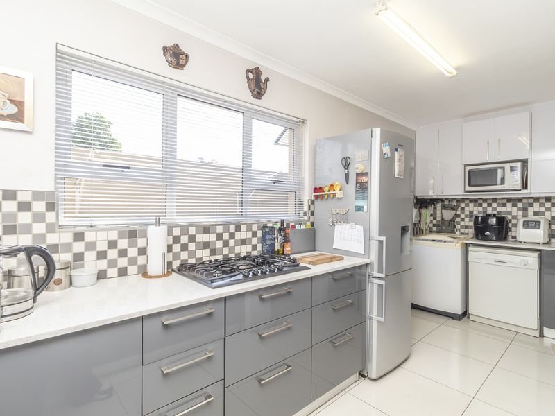 A functional kitchen featuring grey gloss cabinetry, stone benchtops, a gas cooktop, and a tiled splashback with integrated laundry space.