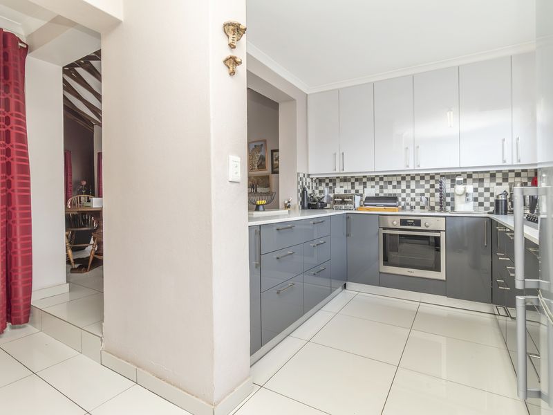 Modern kitchen featuring glossy grey and white cabinetry, a built-in oven, a checkered tile backsplash, and clean tiled flooring.