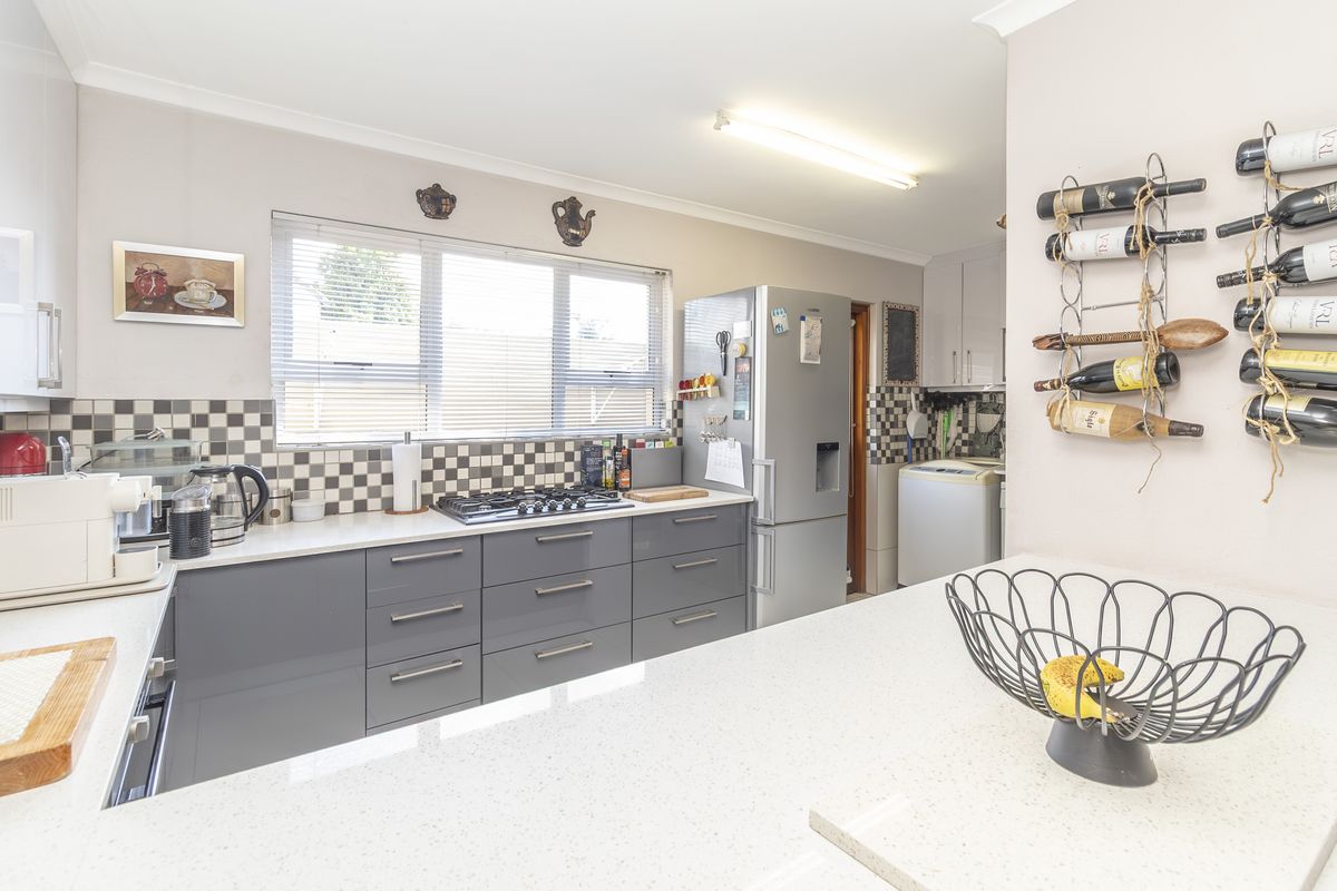 Modern kitchen featuring grey cabinetry, stone countertops, a gas cooktop, and a distinctive checkered tile backsplash, with an adjacent laundry area visible.